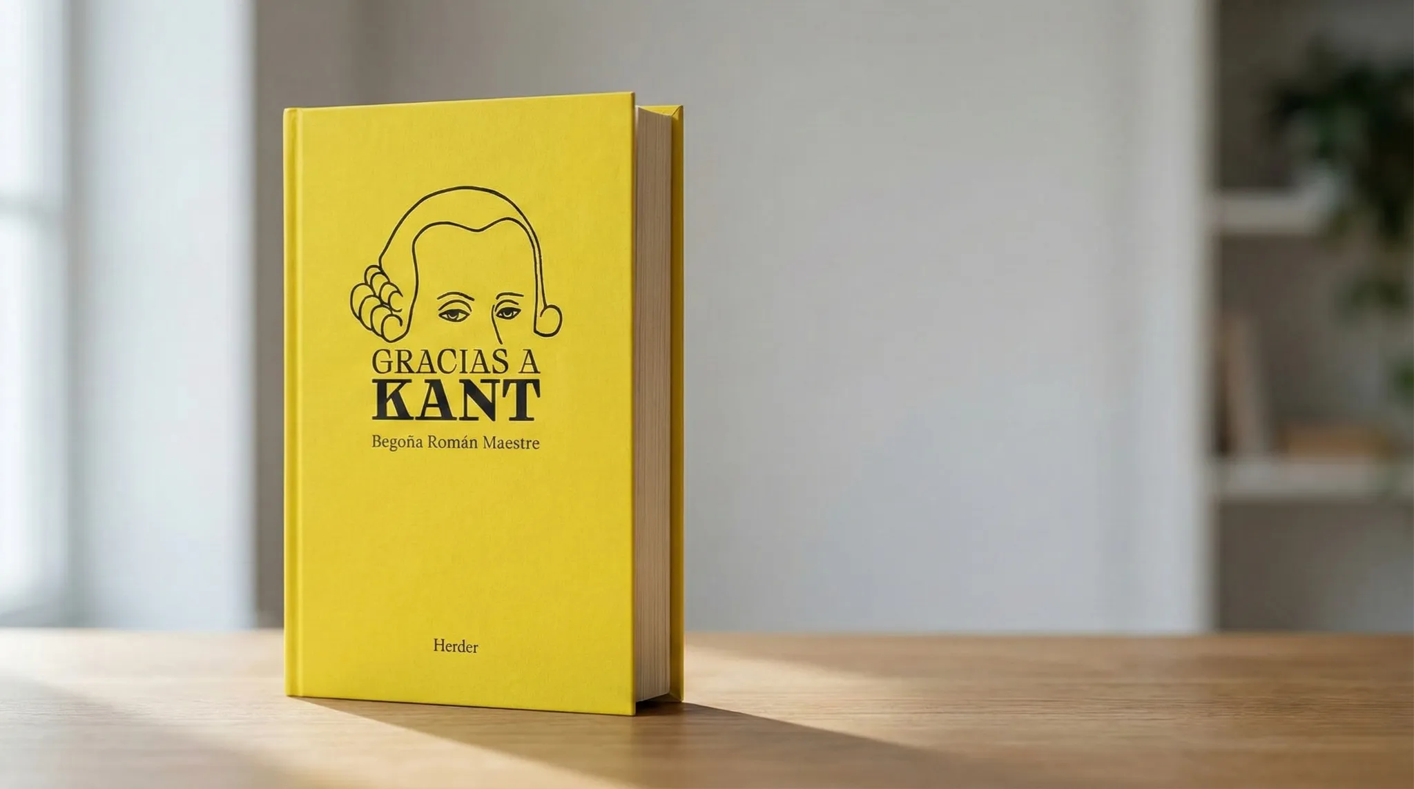 Libro Gracias a Kant de Begoña Román Maestre, con portada amarilla y diseño sobrio, apoyado sobre una mesa de madera en un espacio silencioso que evoca lectura y reflexión.